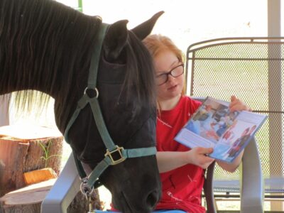 Christina reading a book to a horse